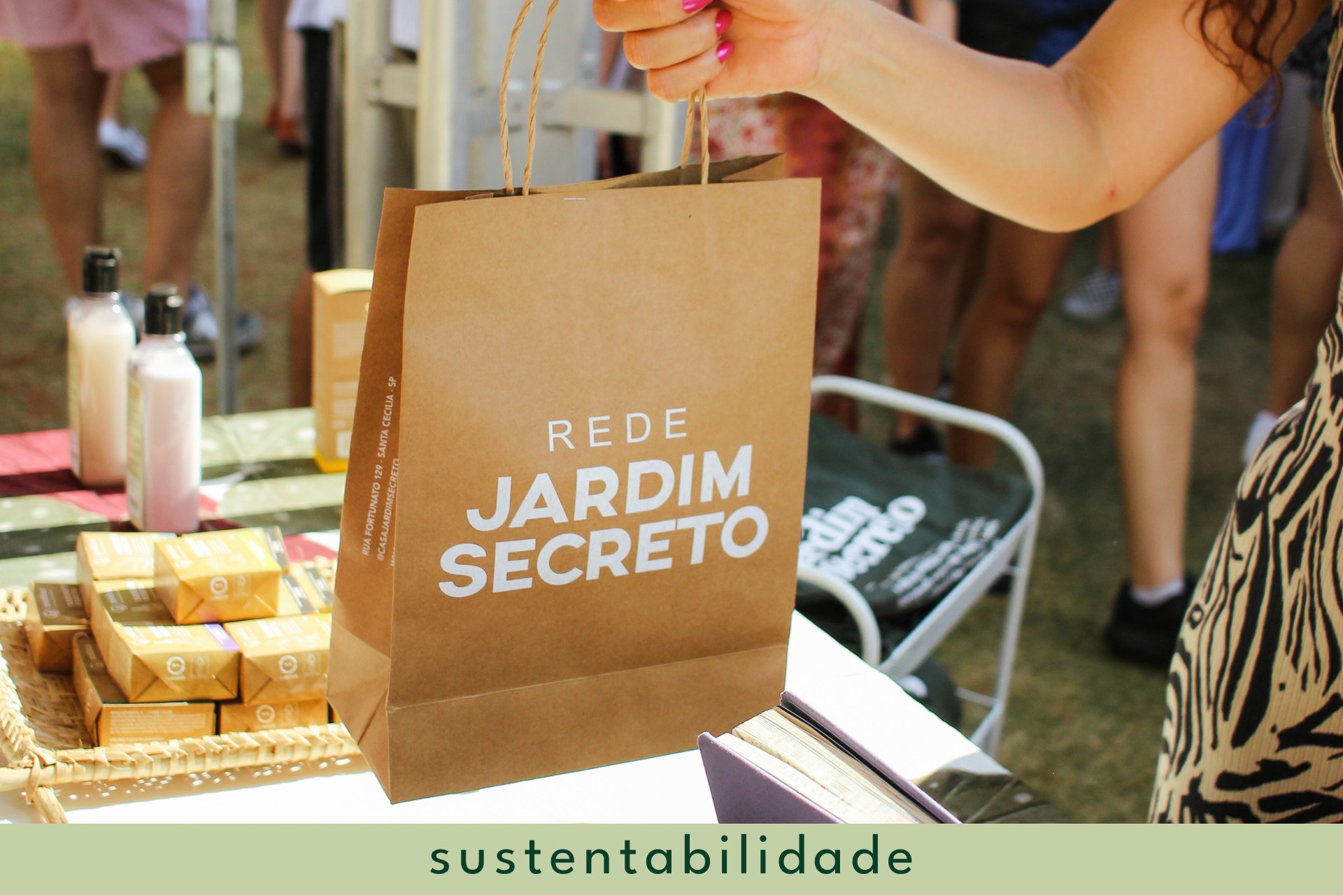 Uma mão segurando uma sacola de papel personalizada escrito "Rede Jardim Secreto"